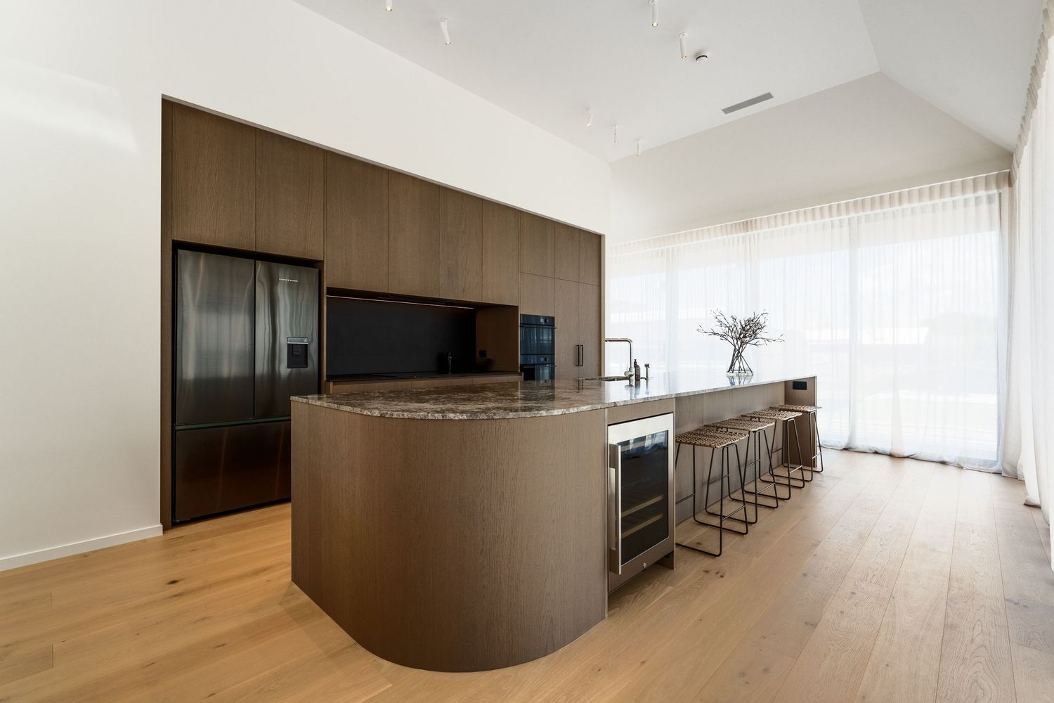 Contemporary open concept living space with curved dark wood accent wall and large windows providing natural light.