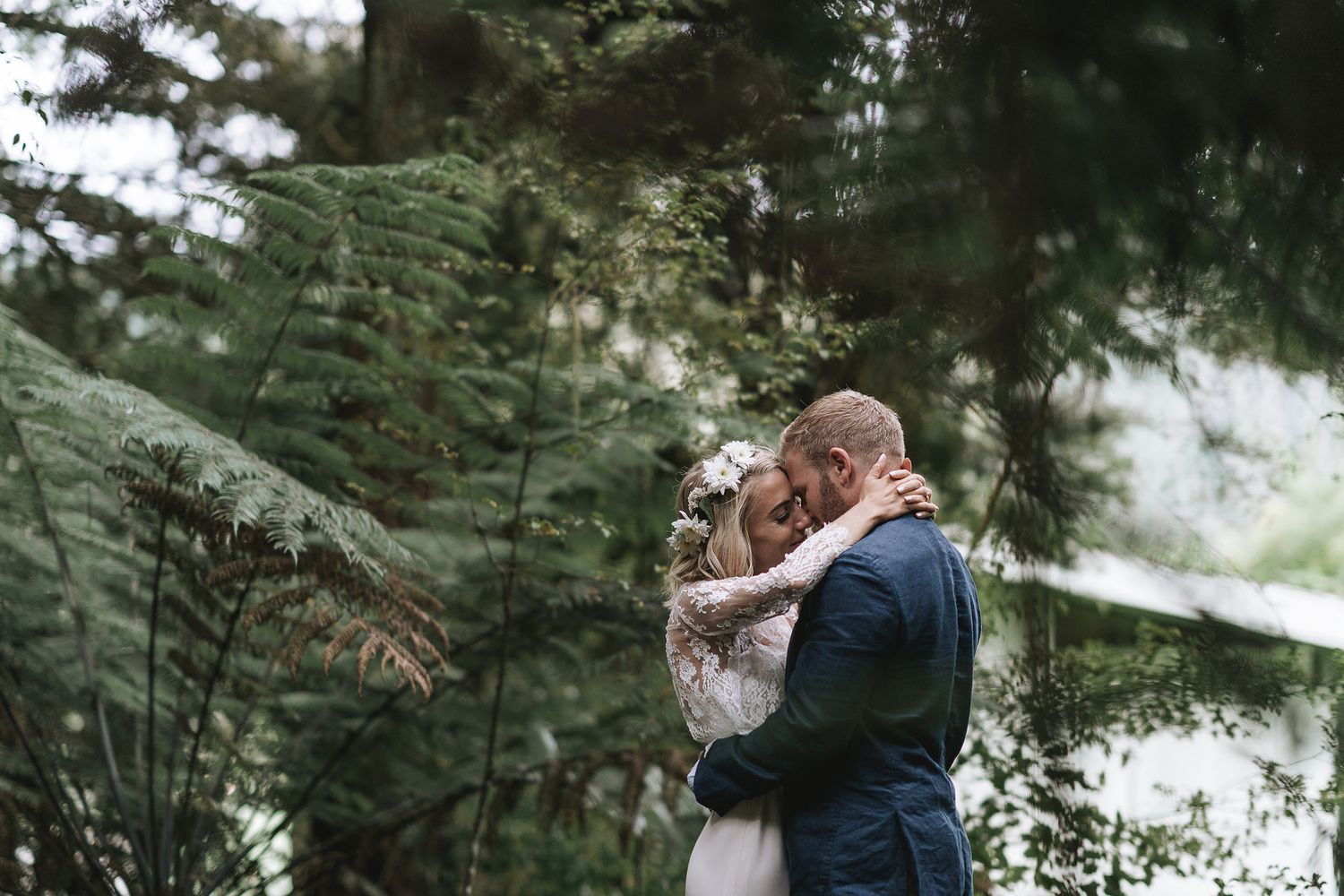 Two people embrace in a romantic moment among evergreen trees in a moody forest setting.