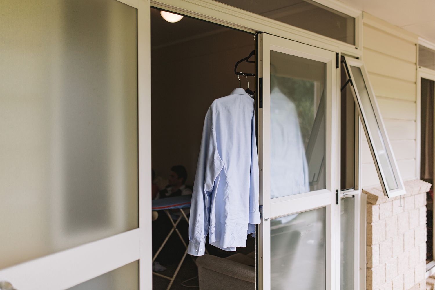 Blue dress shirt hanging outside glass sliding door of residential home porch area.