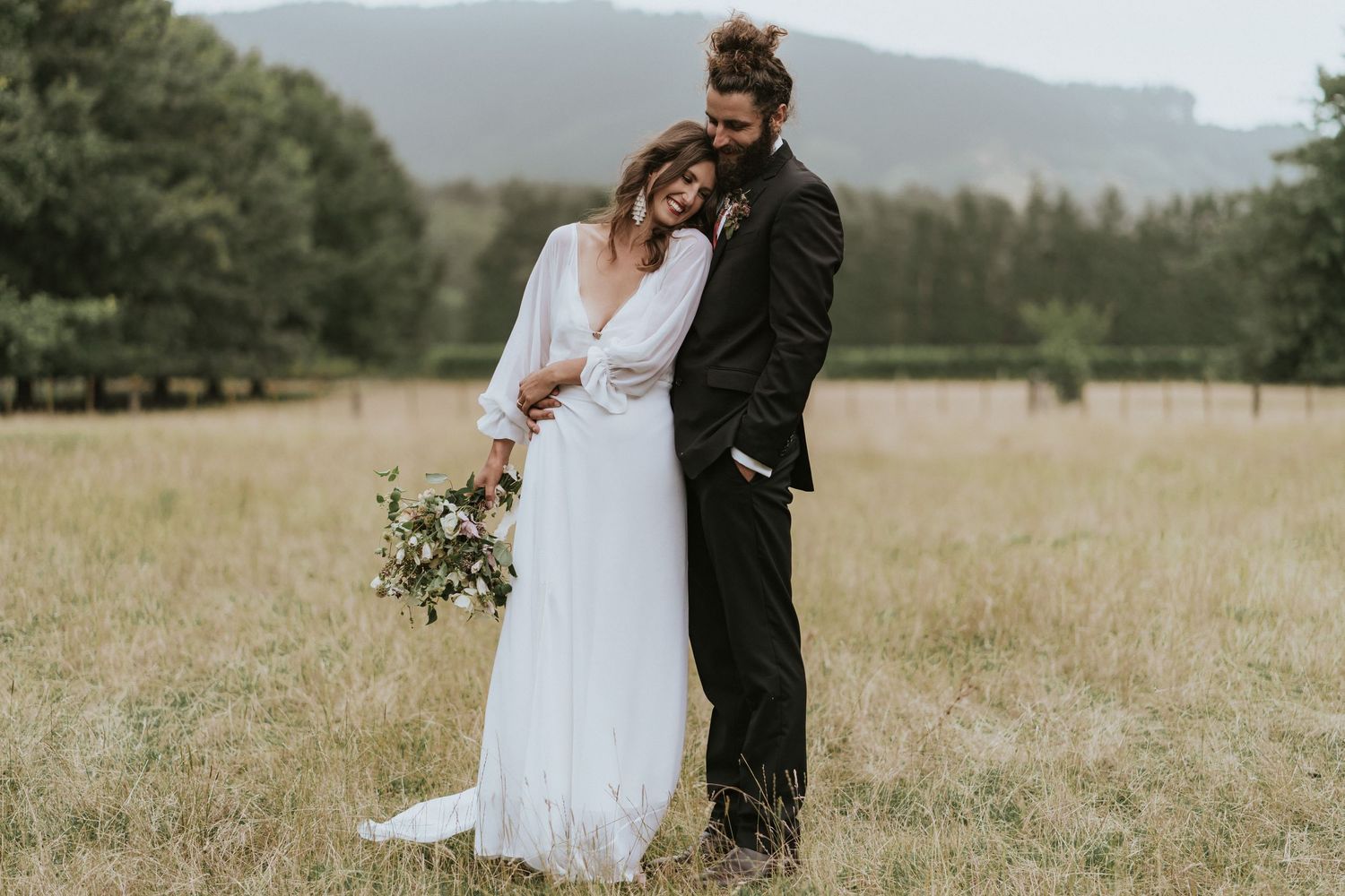 A romantic outdoor wedding scene in a golden field with mountains in the background.