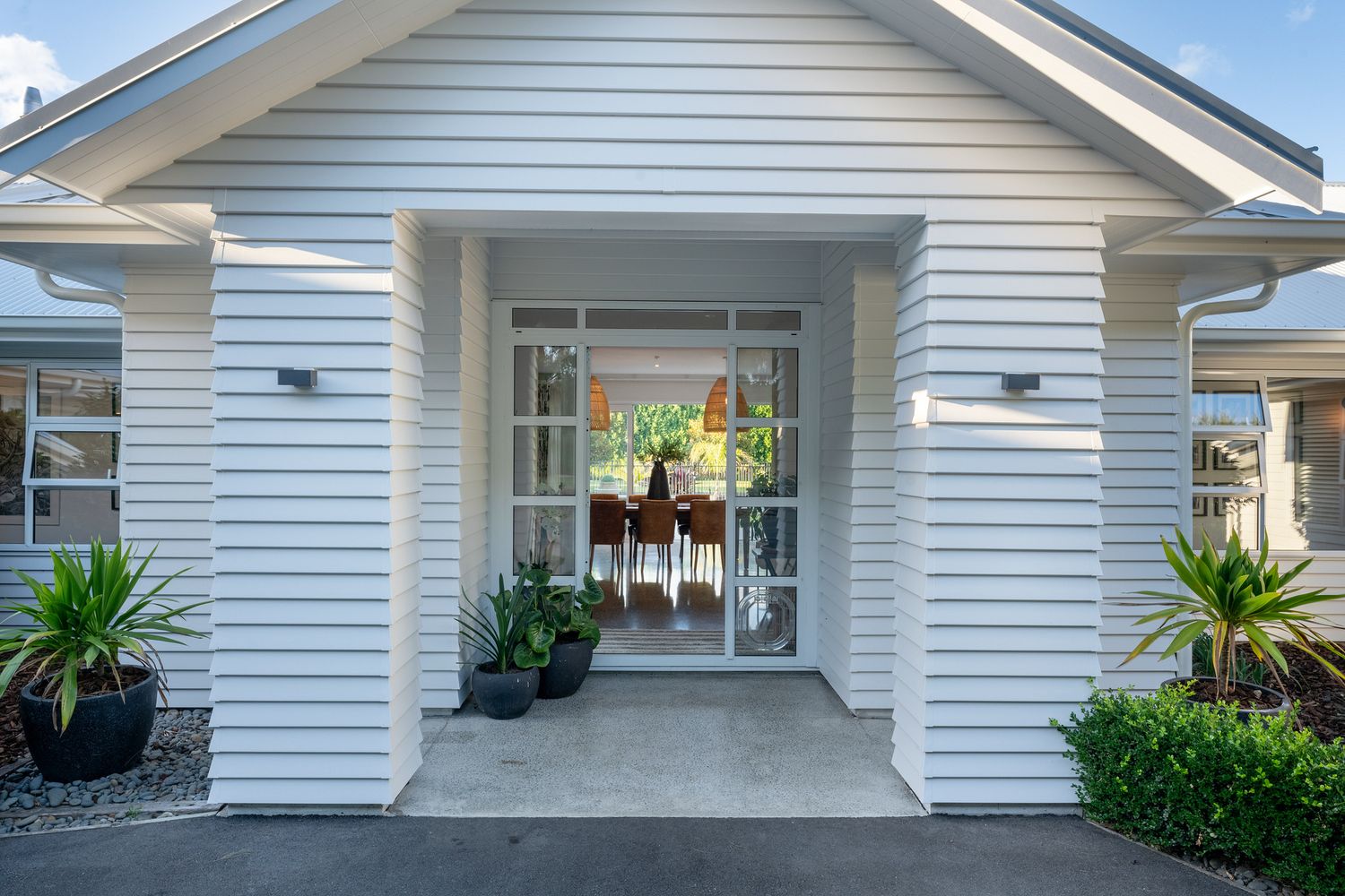 Elegant white clapboard home entrance with glass doors and potted plants on the porch.