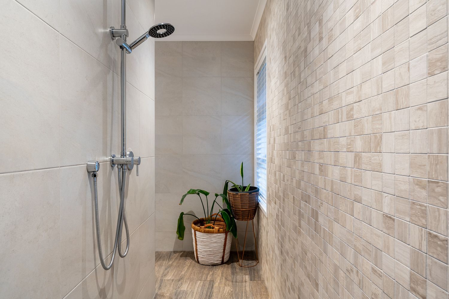 Minimalist walk-in shower with beige tile walls, window, and decorative potted plants.