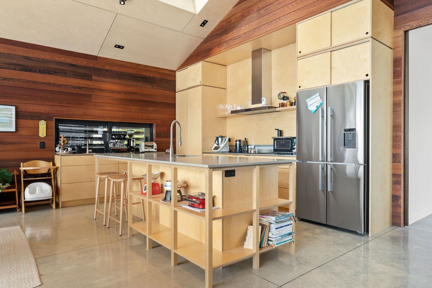 Modern open concept kitchen with light wood cabinets, stainless steel appliances and wooden wall paneling.