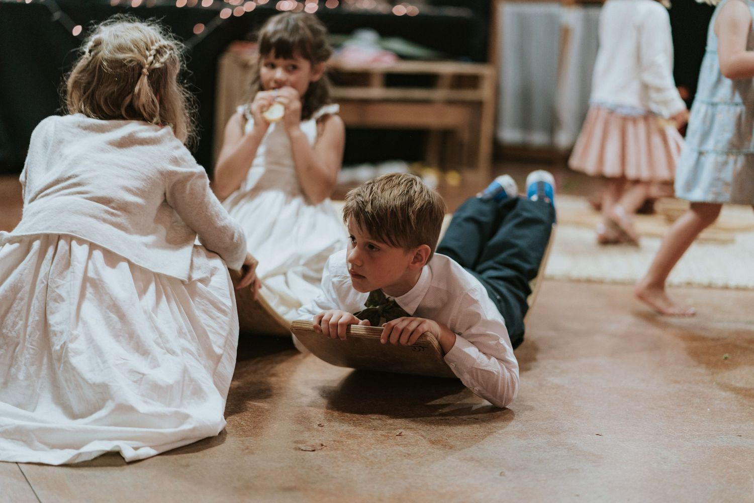 Low angle view of children sitting on wooden floors playing with hands and toys in a warm-lit indoor setting.