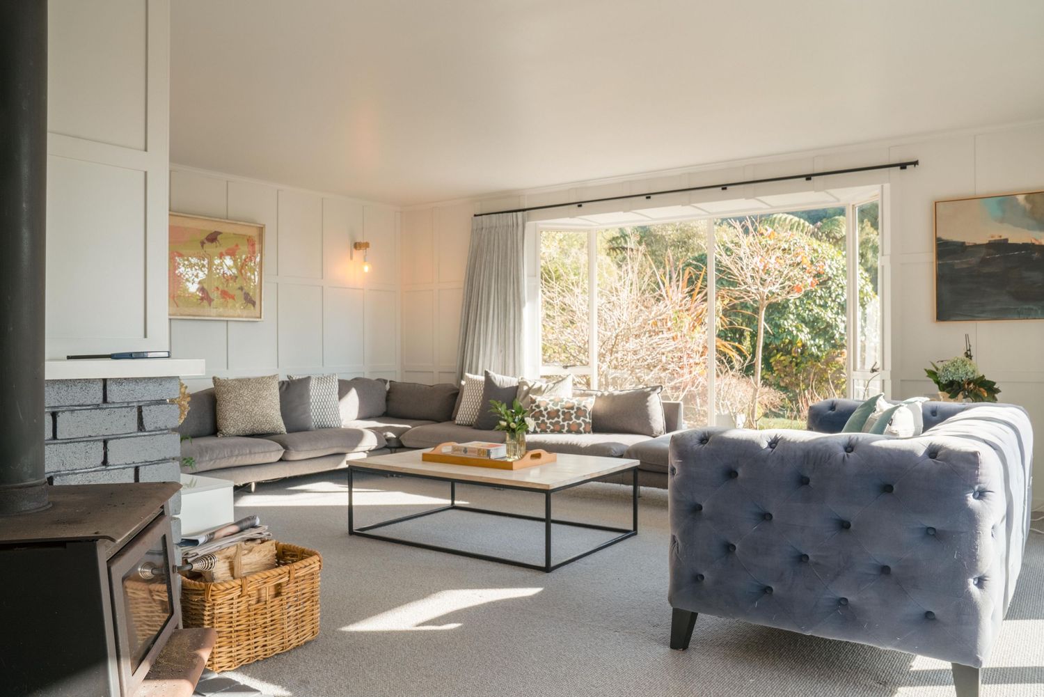 Modern living room with gray tufted sofa, black coffee table and white walls filled with natural light through windows.