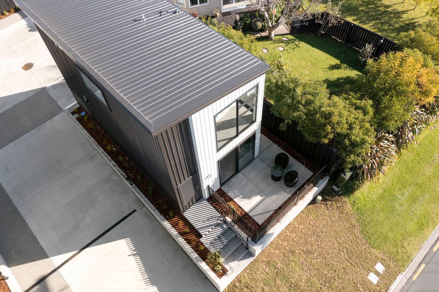 Aerial view of modern home exterior with dark metal roof and white walls featuring a small patio deck.