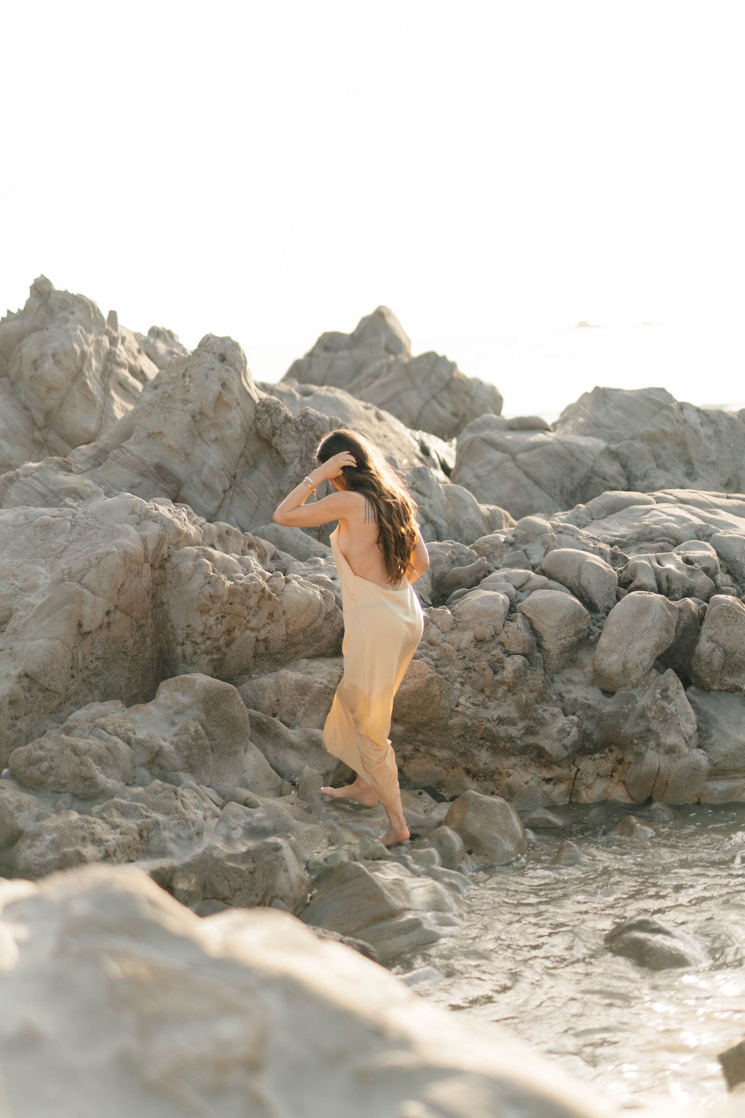 Person in light clothing exploring rocky coastal formations during sunset.