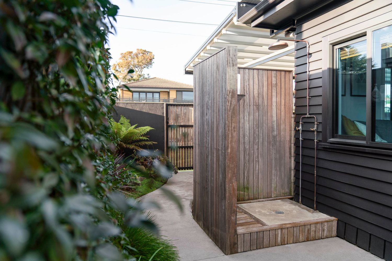 Wooden pathway leading to a timber-clad entrance between modern black weatherboard walls.