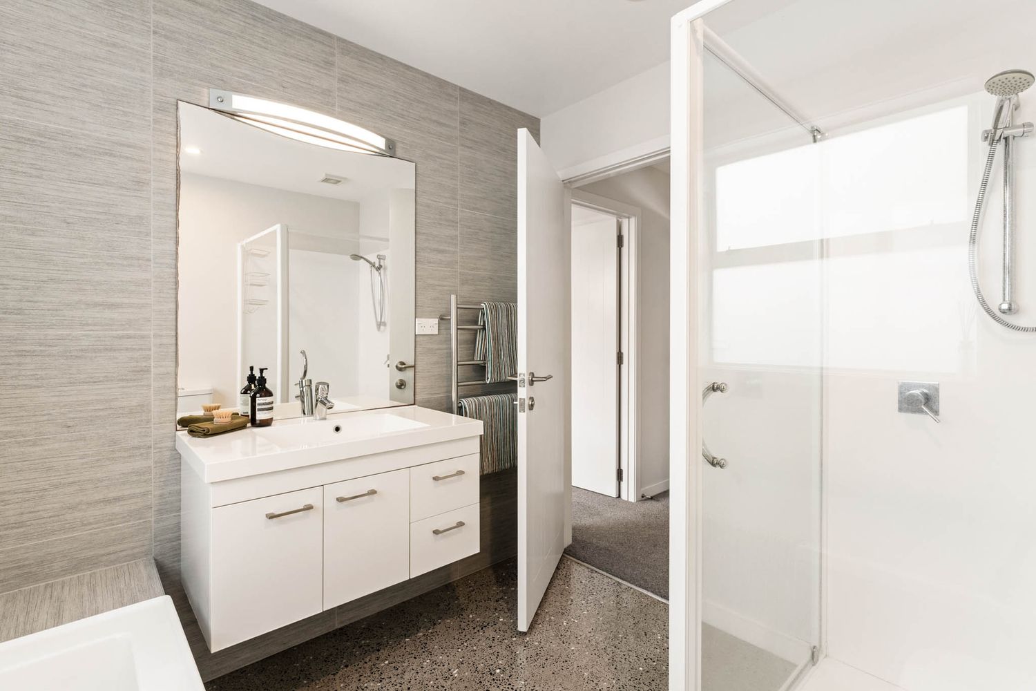 Contemporary bathroom with white vanity, grey textured walls, and glass shower enclosure features modern fixtures.