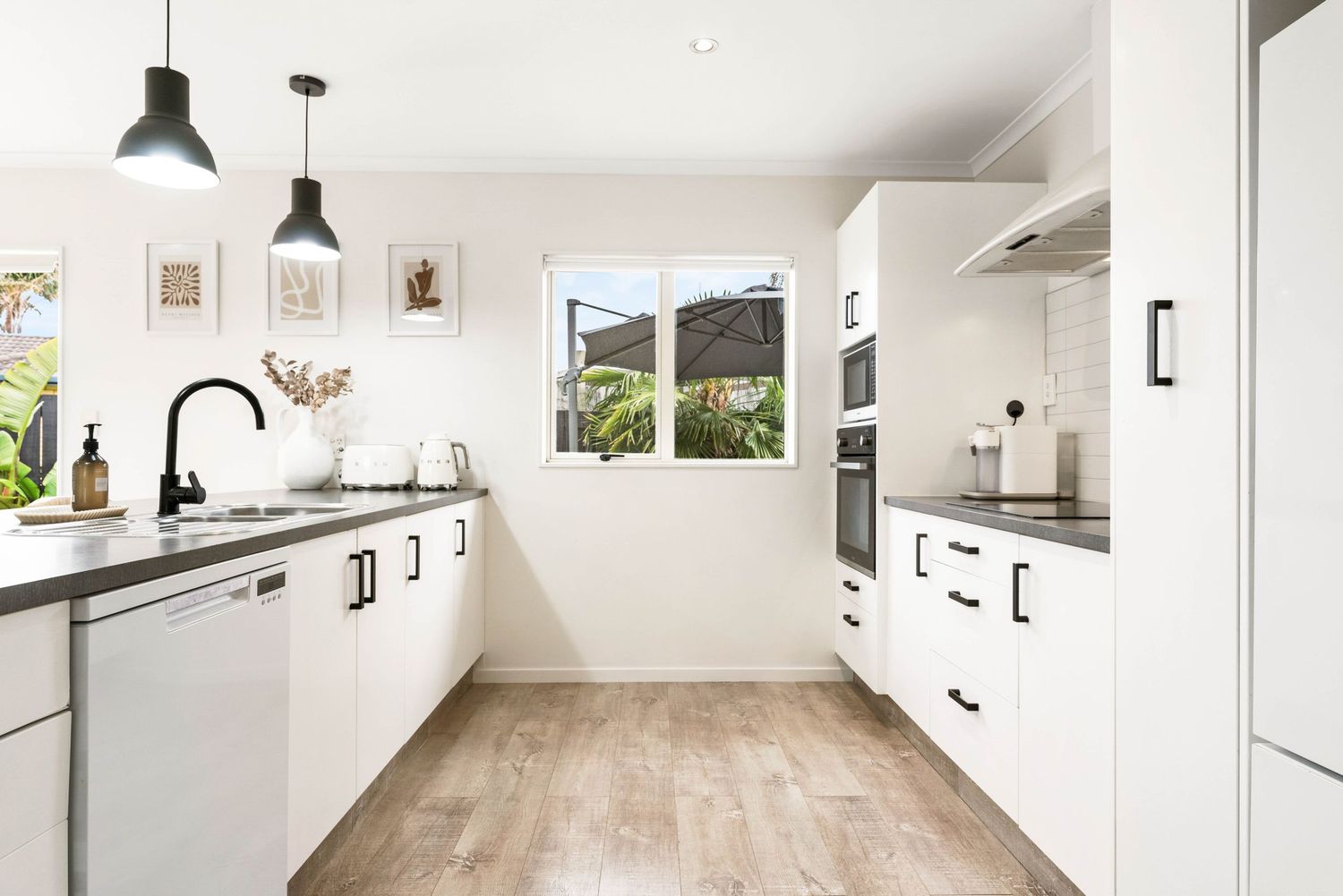 Clean white modern kitchen with black pendant lights and hardwood flooring.