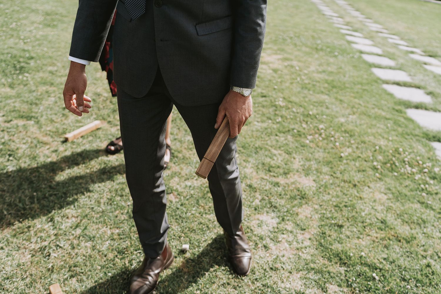 Person in formal black suit holding a book stands on a grass lawn with stepping stones path.