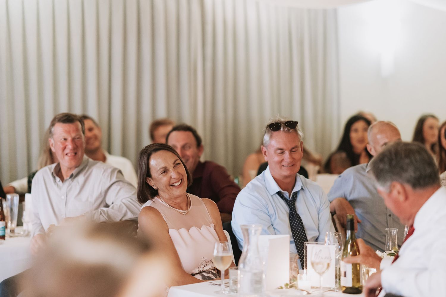 Wedding guests enjoying themselves and laughing during reception dinner at tables with white tablecloths.