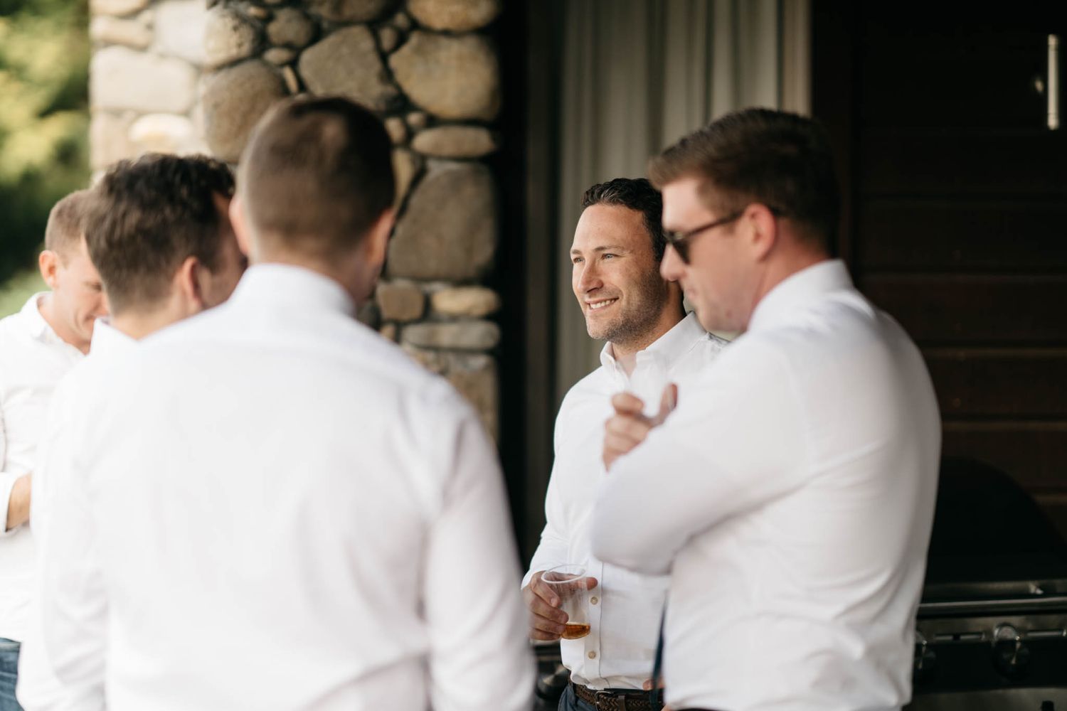 A group of groomsmen in white shirts sharing a lighthearted moment on a stone porch.