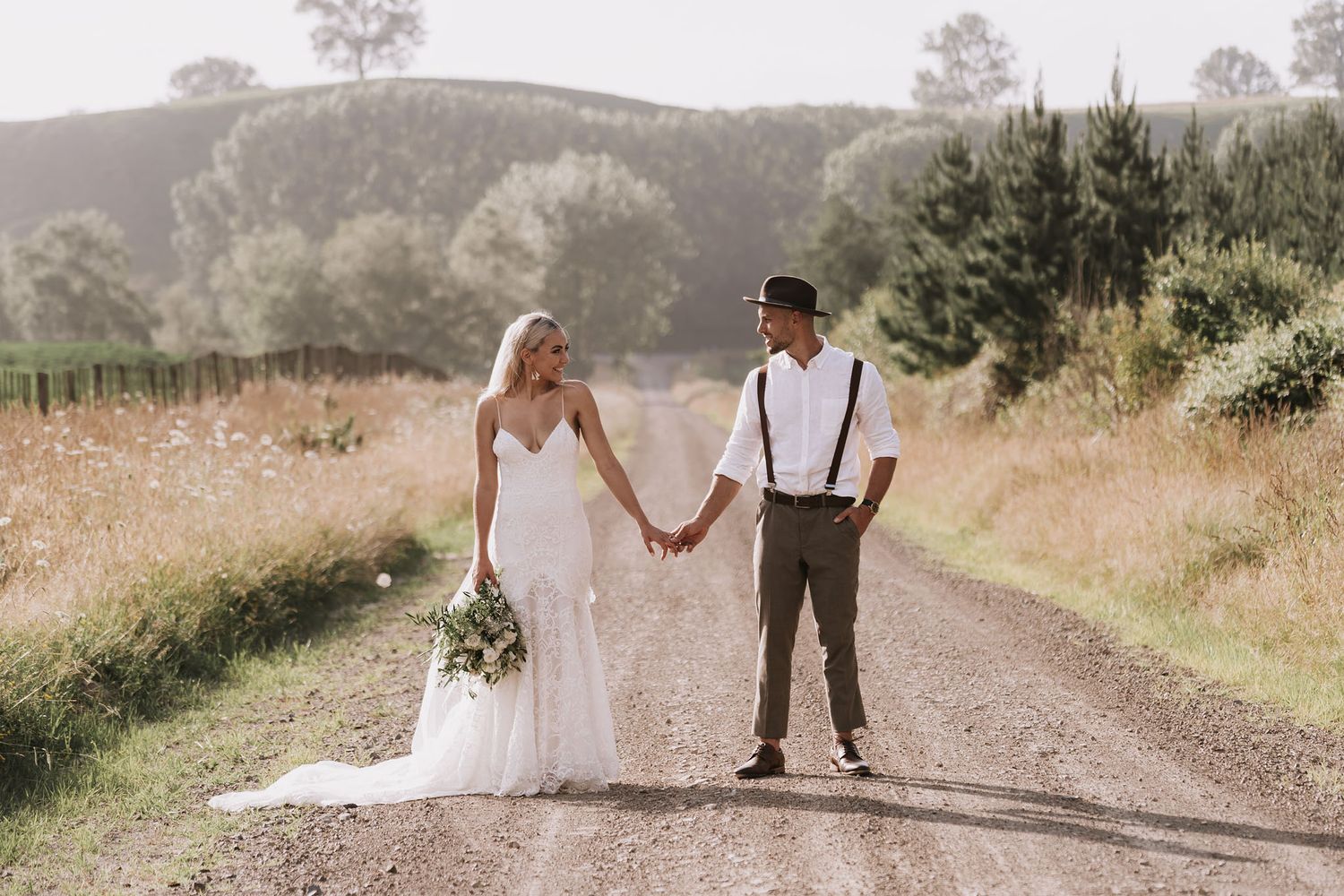 A newlywed couple shares a romantic moment walking together down a winding dirt path in elegant wedding attire.