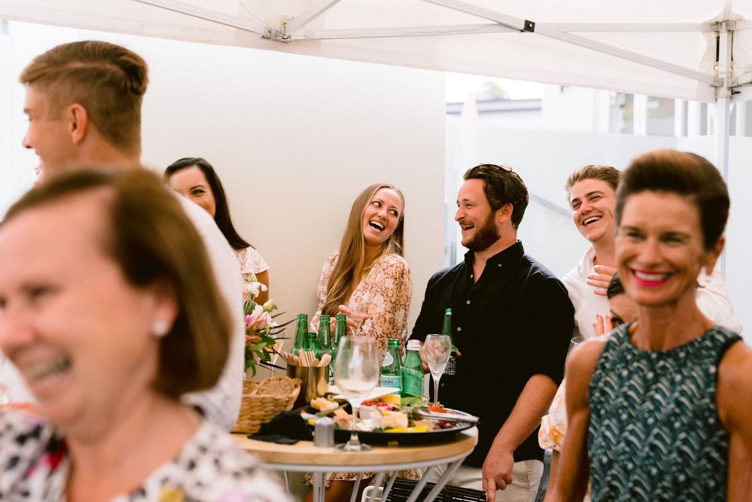 Wedding reception guests enjoying themselves under a white tent at an outdoor celebration.