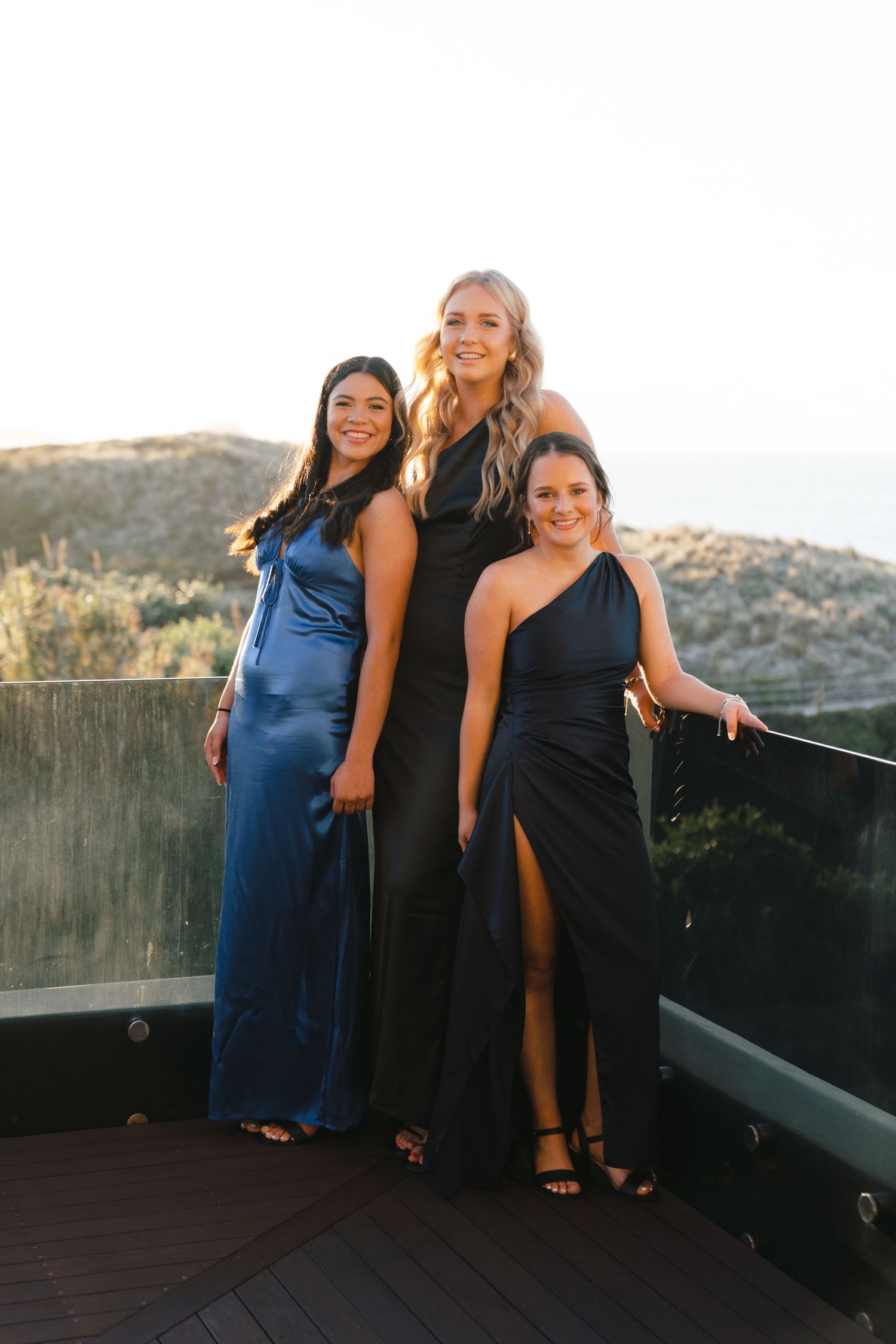 Group photos on outdoor deck at sunset with people wearing formal blue and black dresses.