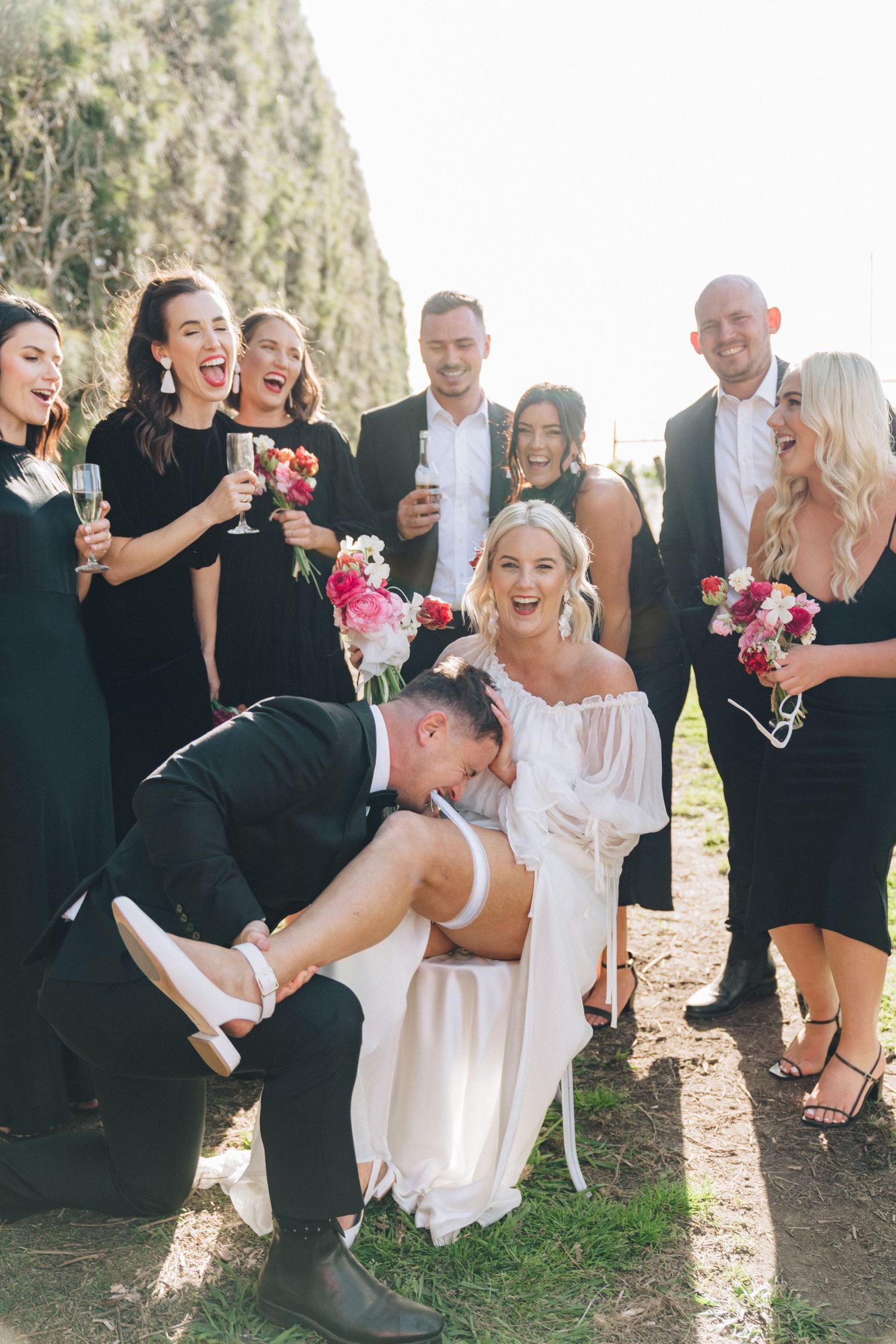 Wedding party in black and white attire shares joyful candid moments during outdoor photo session.