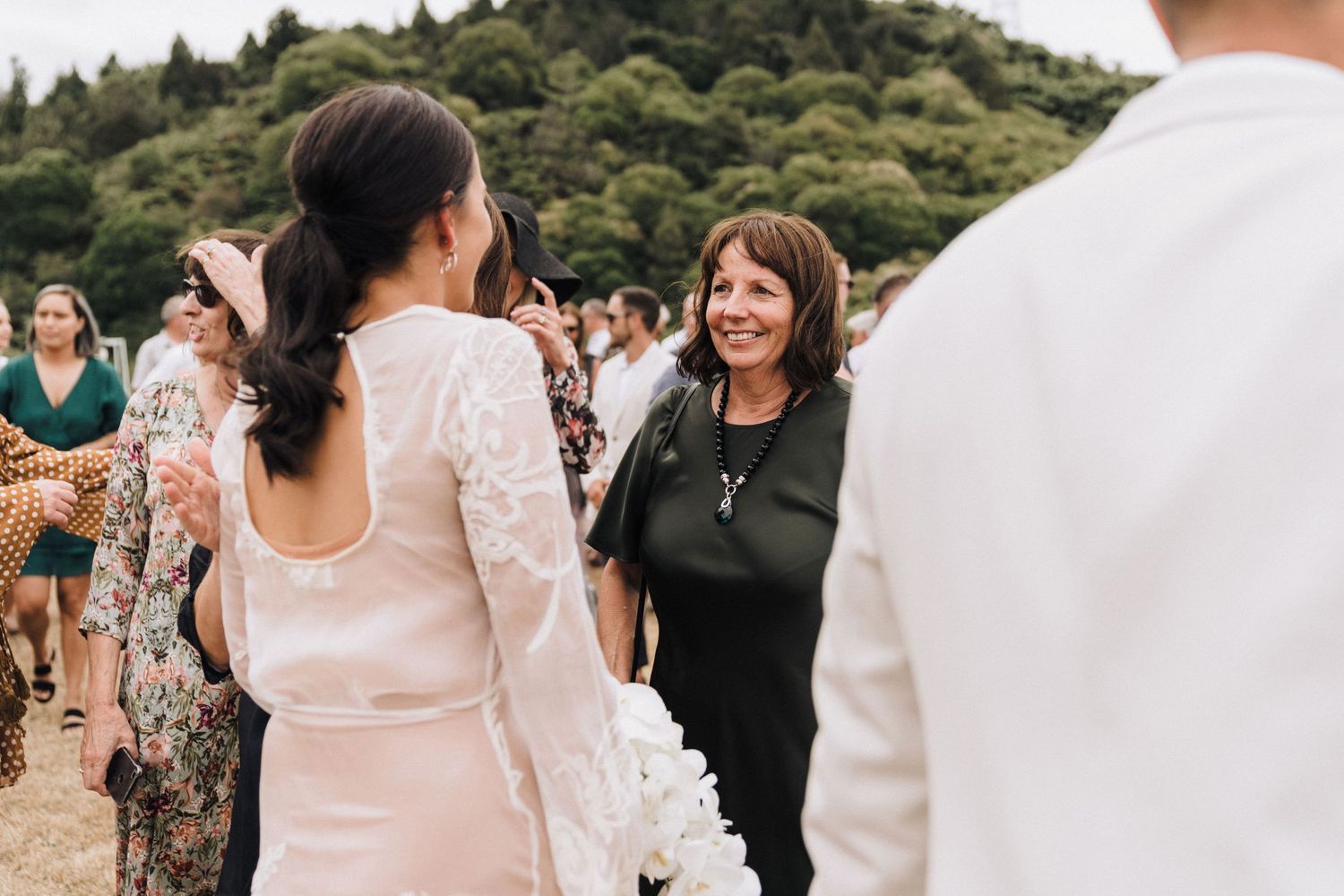 Outdoor wedding gathering with guests mingling in natural setting with hills in background.