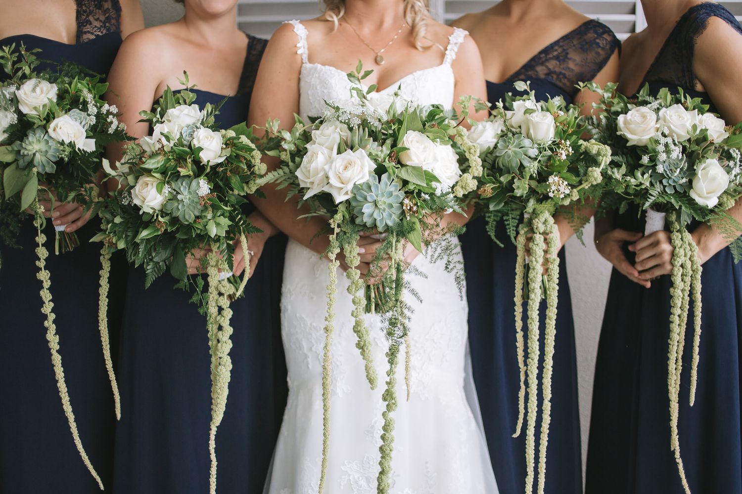Navy-clad wedding party holds long cascading white and green floral bouquets in elegant formal lineup.