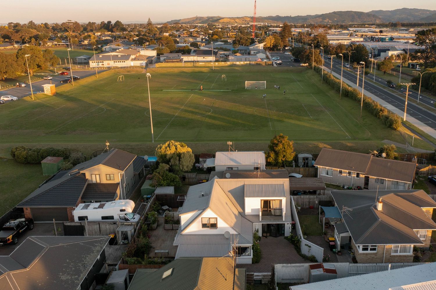 Panoramic aerial drone view of suburban homes and athletic fields at sunset with mountains in the background.