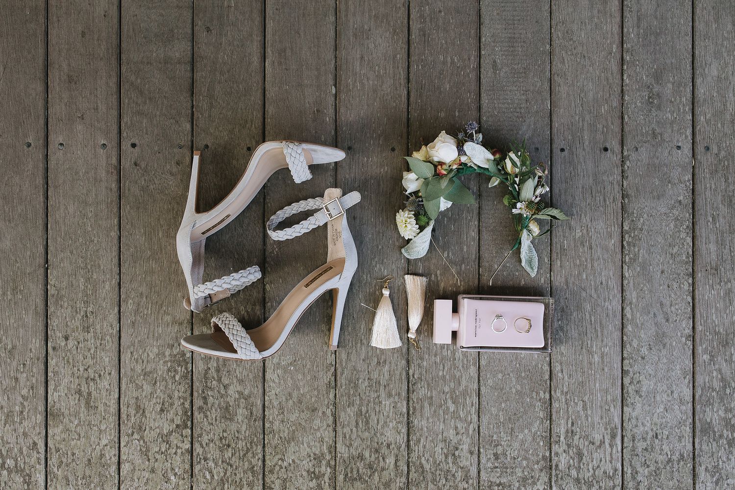 Elegant silver bridal heels displayed with white flowers, perfume bottle and wedding accessories on rustic wooden floor.