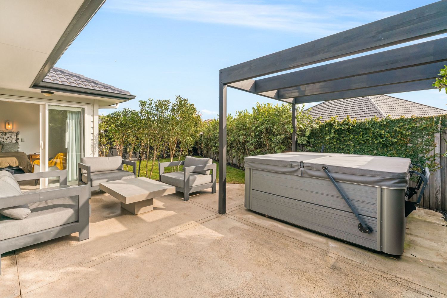 Modern outdoor patio area with loungers and hot tub under a sleek pergola cover with garden views.