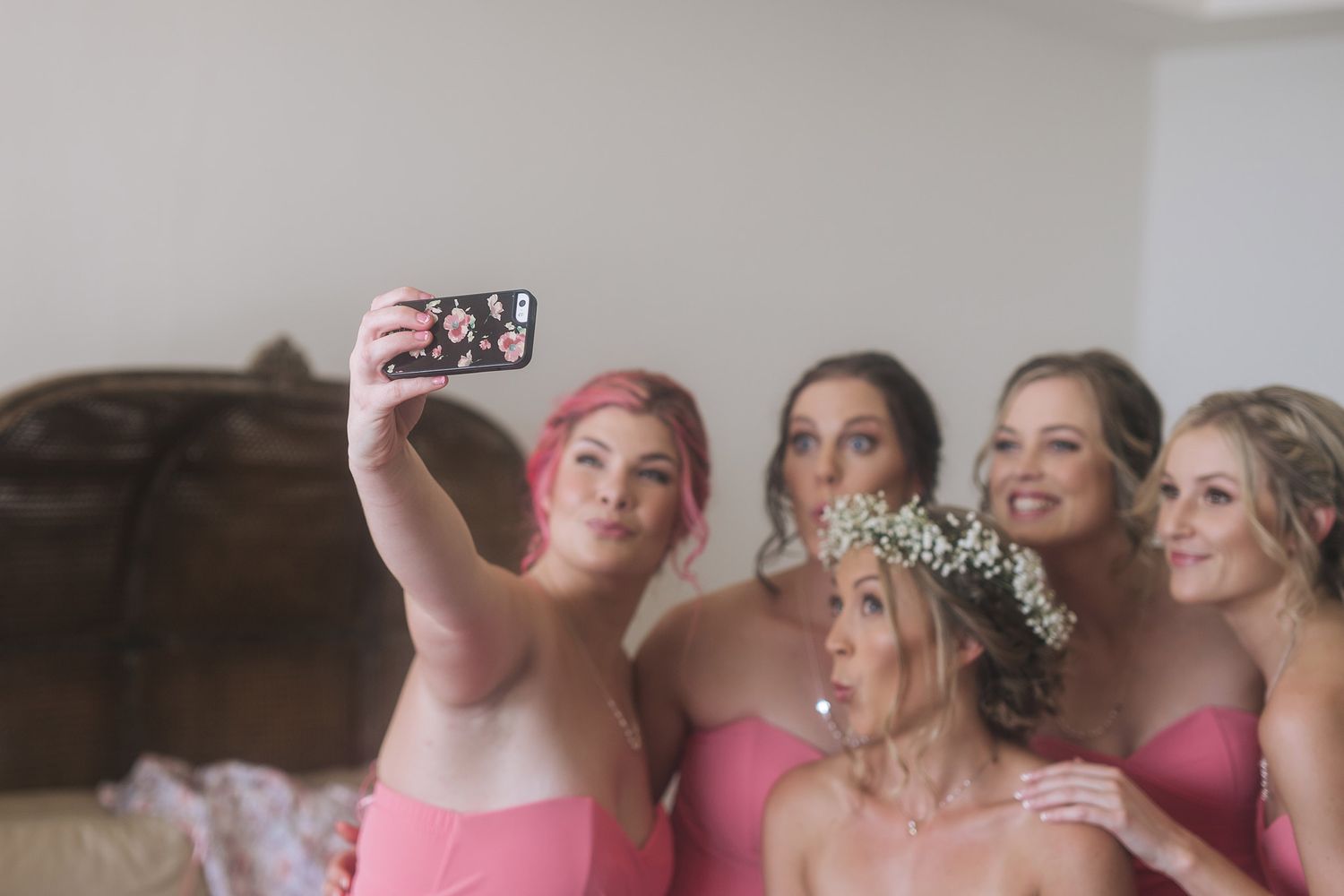 Group wearing pink dresses taking selfie photo together while smiling and laughing.