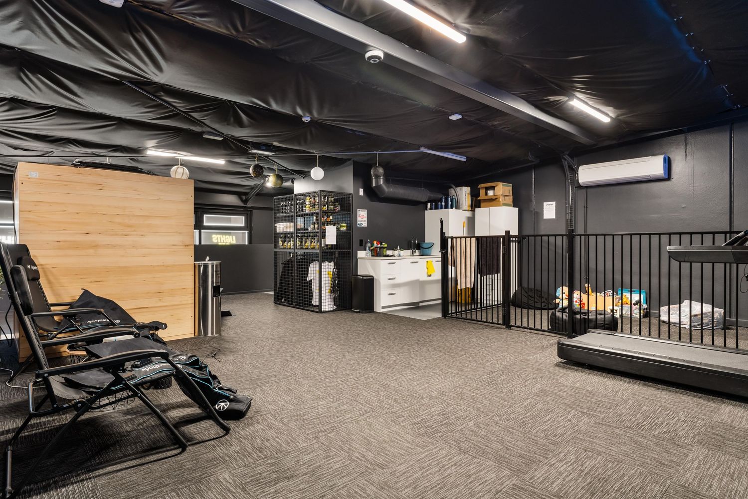 Modern fitness studio space with carpeted floor, black chairs, and exposed ceiling design.