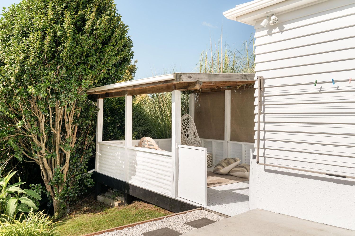 White outdoor porch with wooden beams and lush greenery creating a cozy coastal retreat.