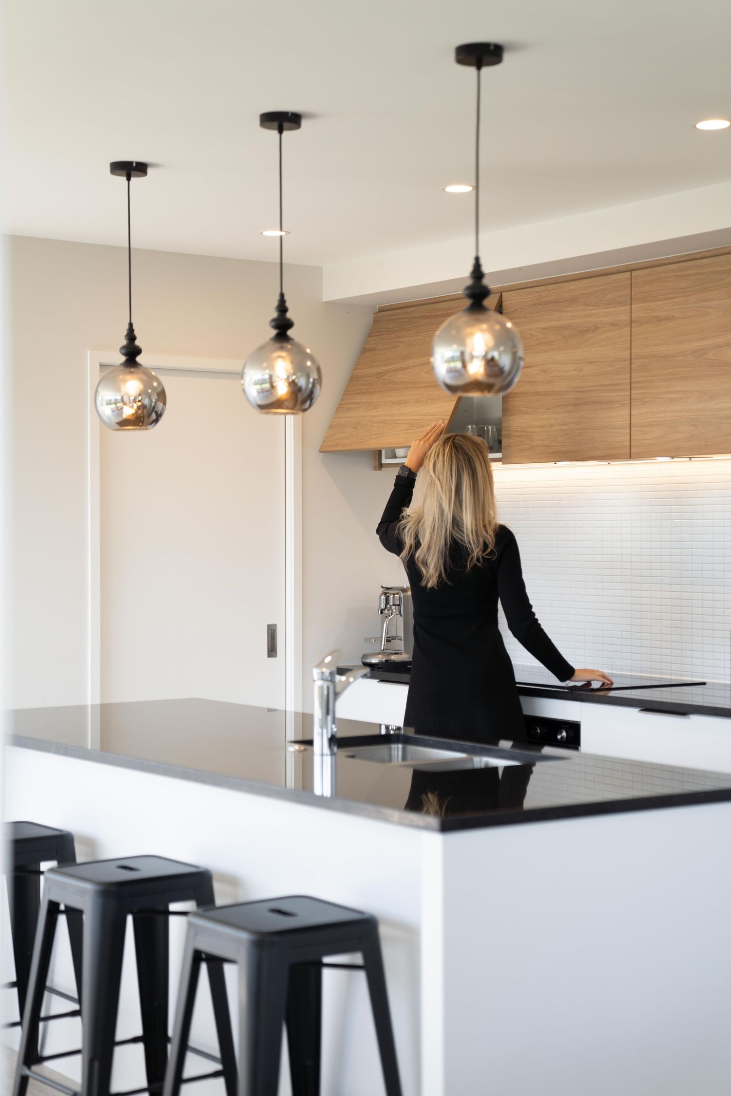 Sleek kitchen counter with black bar stools and glass pendant lights in a contemporary home setting.