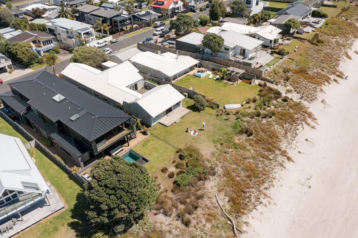 Aerial view of beachfront homes and properties along a sandy coastline showing waterfront real estate and landscaped yards.