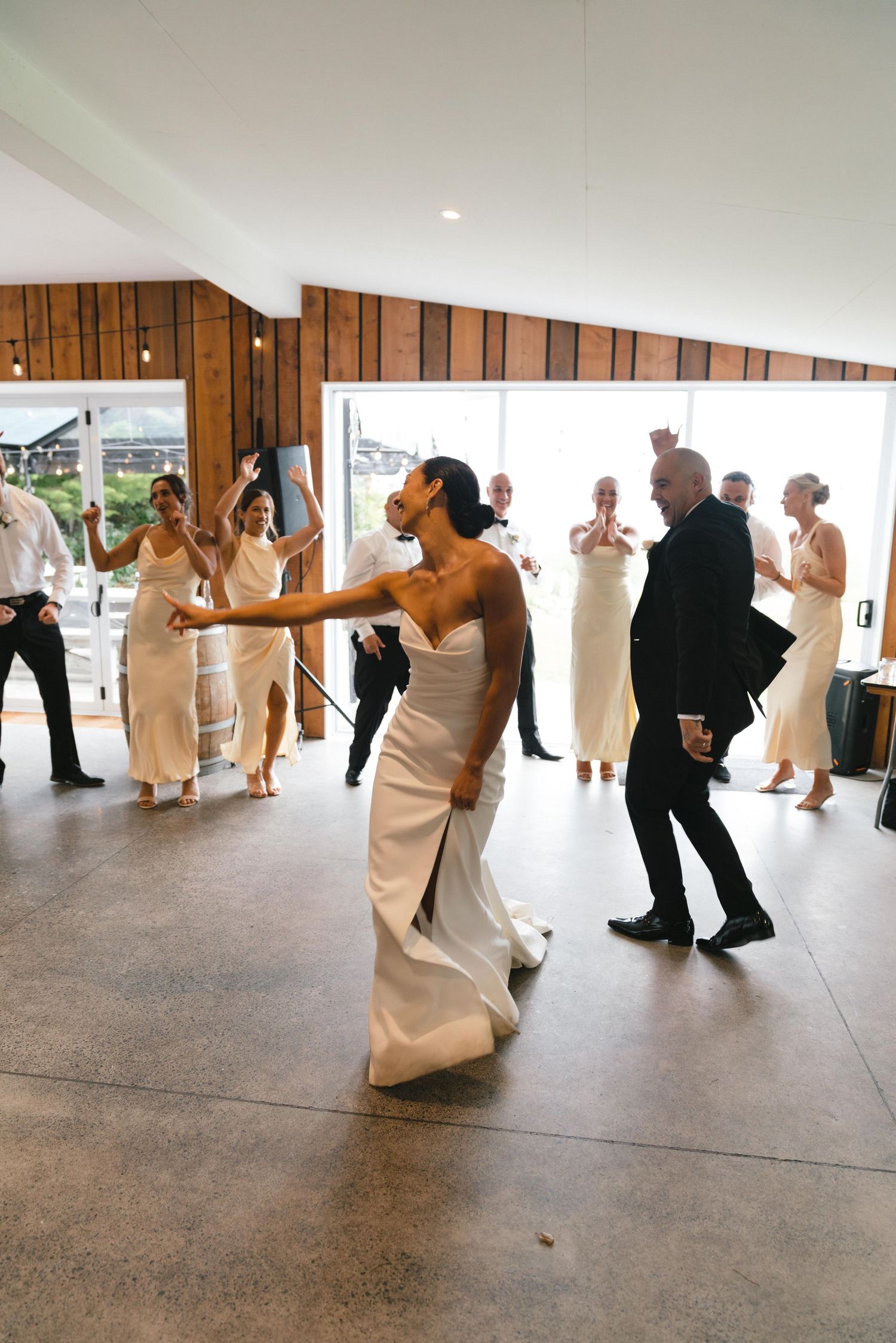 Guests dance and celebrate during a wedding reception in a modern venue with wood-paneled walls and sloped ceiling.