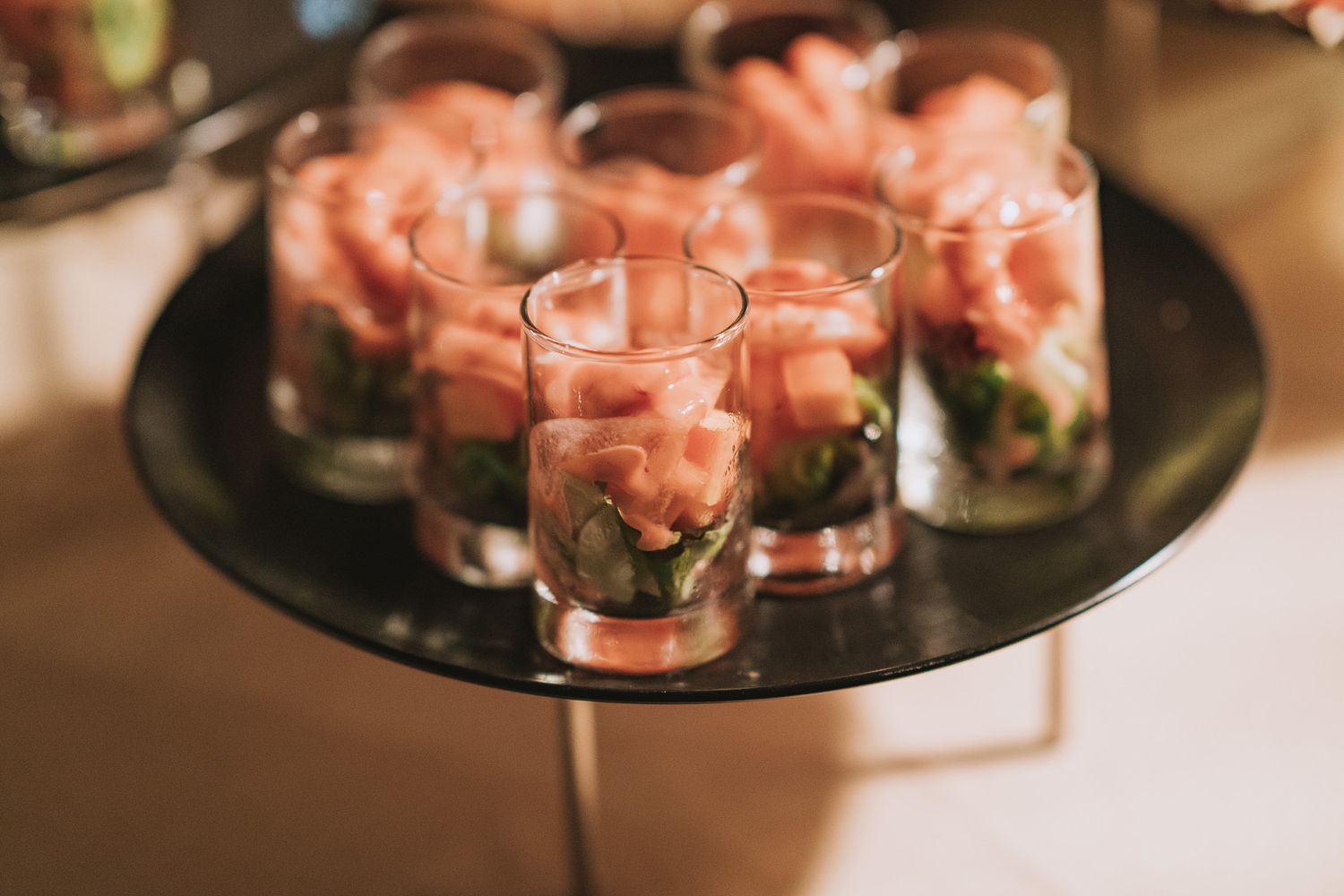 Pink flower arrangements in glass vases displayed on a dark circular serving tray.