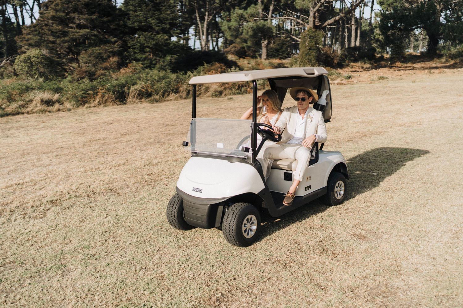 Golf carts transporting wedding guests along a dirt path surrounded by trees.