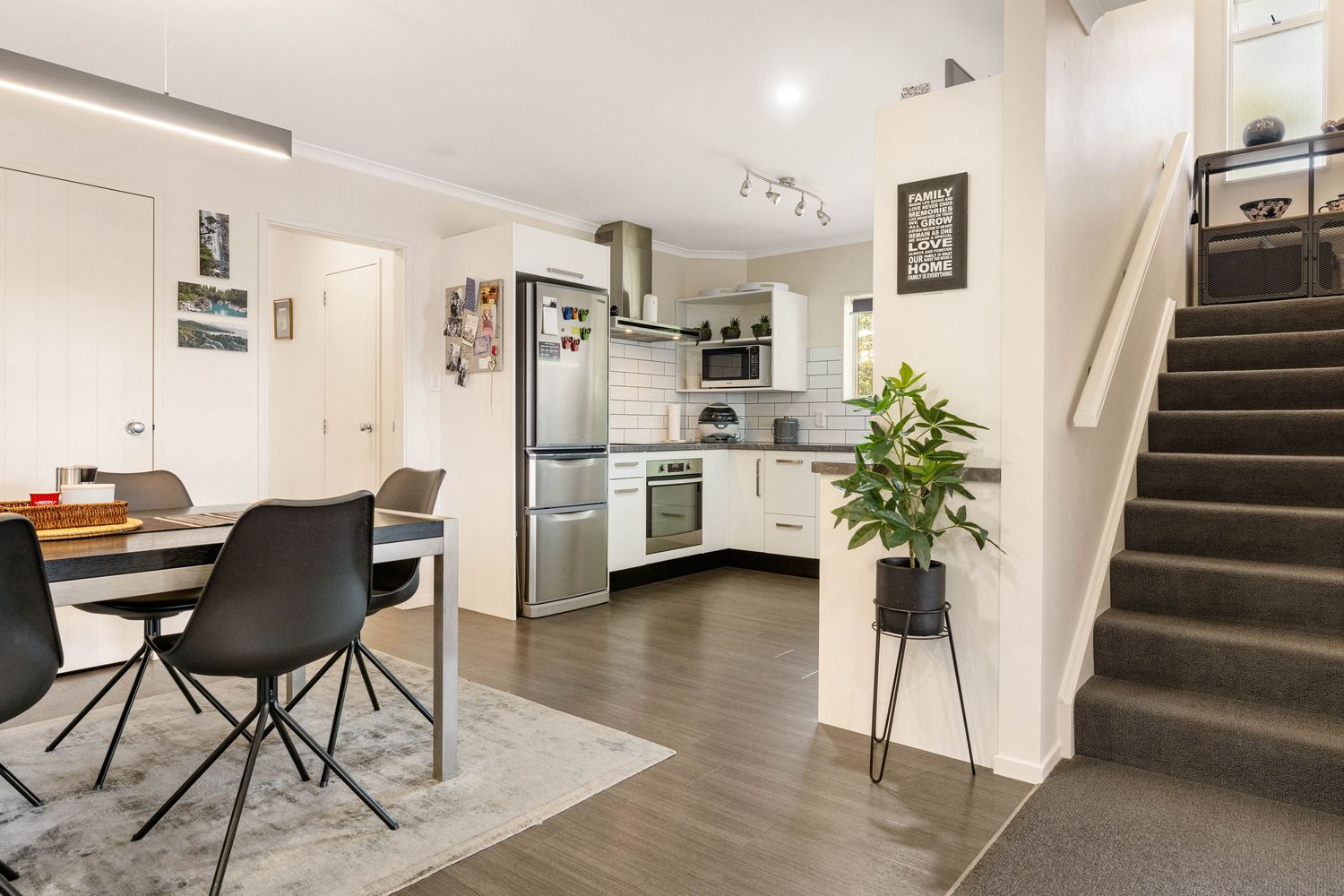 Modern open-plan apartment interior with white kitchen, carpeted stairs, and dark wood flooring.