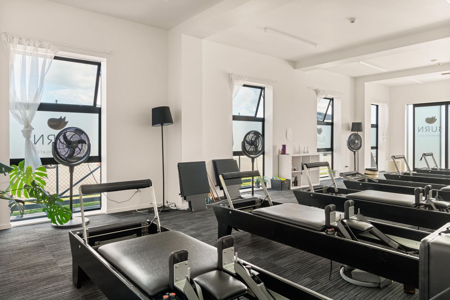 Bright fitness studio with reformer Pilates equipment and large windows letting in natural light.