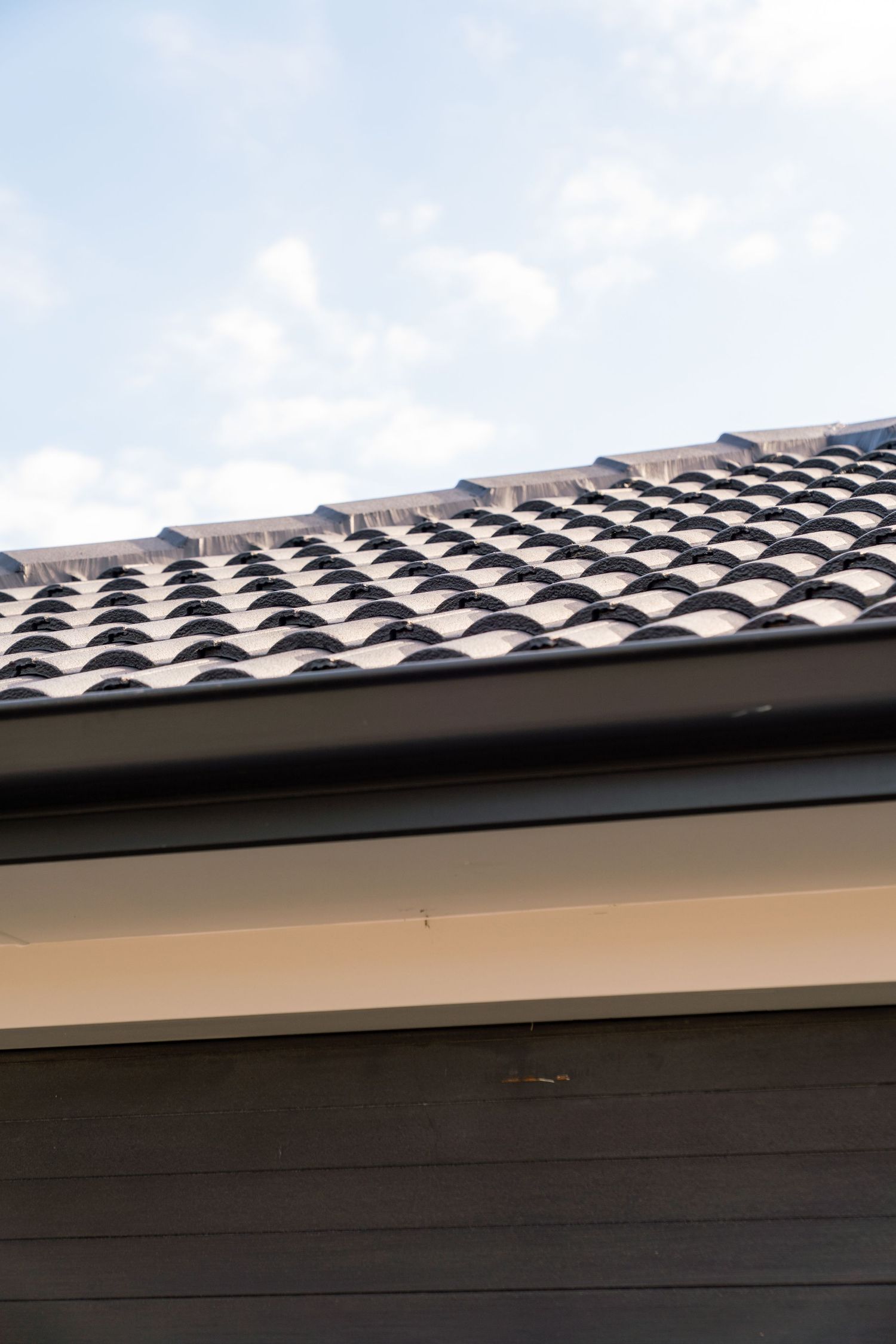Close-up of gray clay tile roofing on a modern house against blue sky.