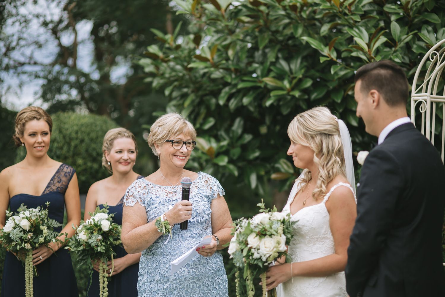 Outdoor garden wedding ceremony with floral bouquets and elegant attire on a beautiful summer day.