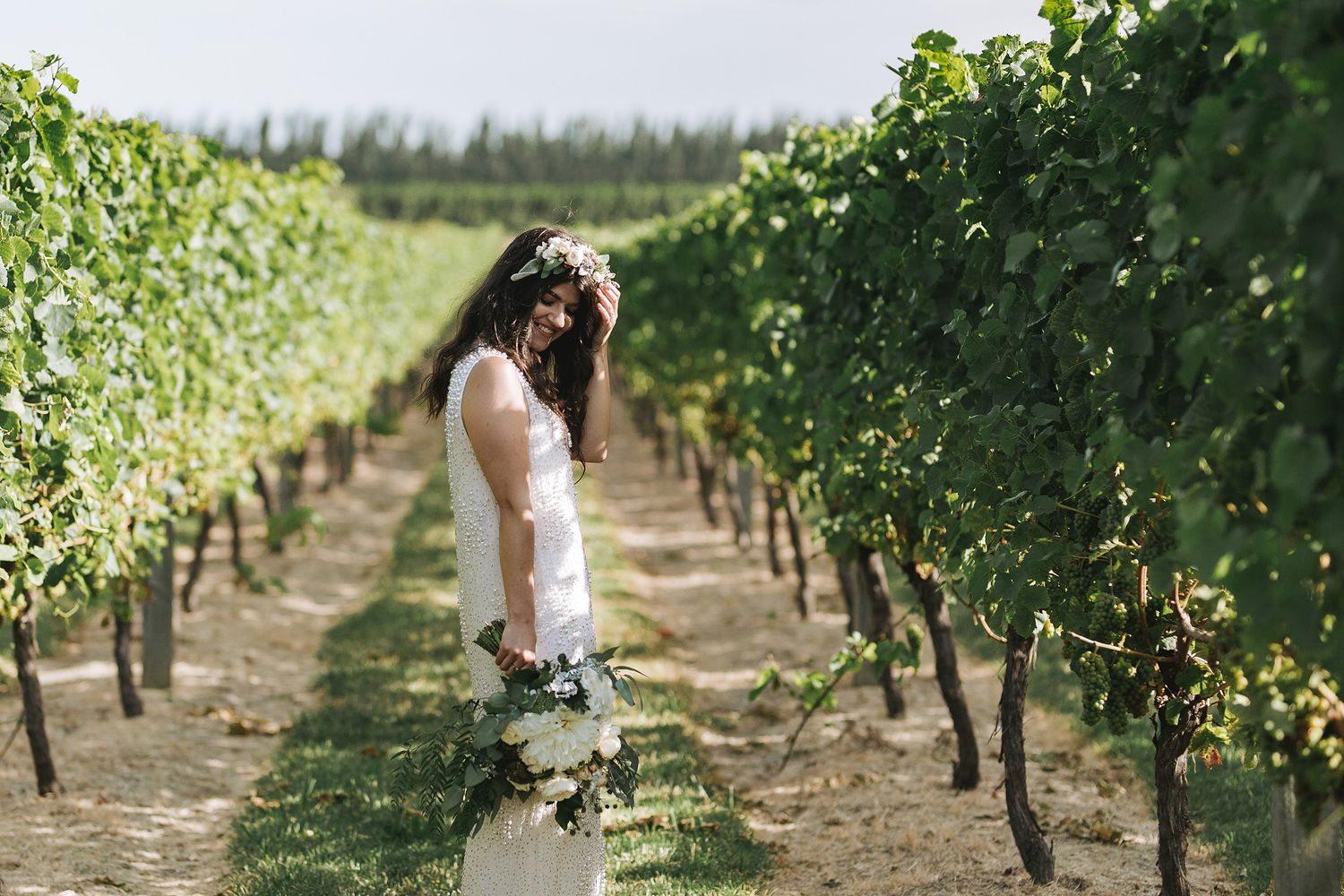 Two white-dressed figures walking down scenic vineyard rows on a sunny day in wine country.