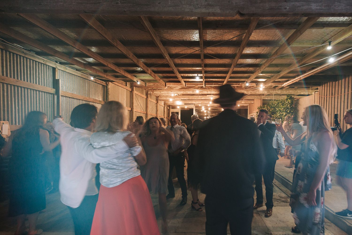 People dancing and celebrating at a lively indoor event with warm industrial lighting and rustic decor.