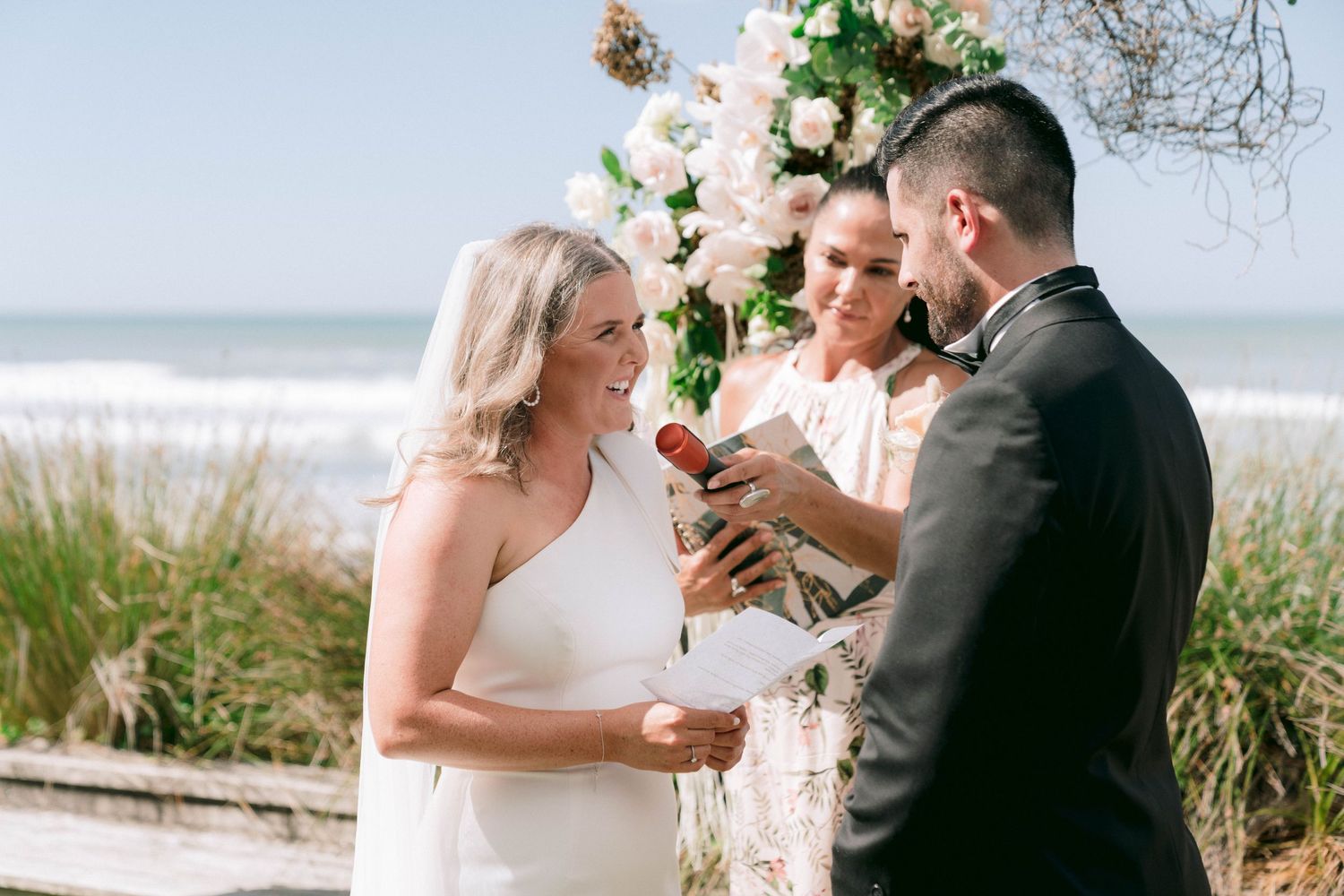 Romantic beach wedding portraits with elegant white floral arrangements along the shoreline.