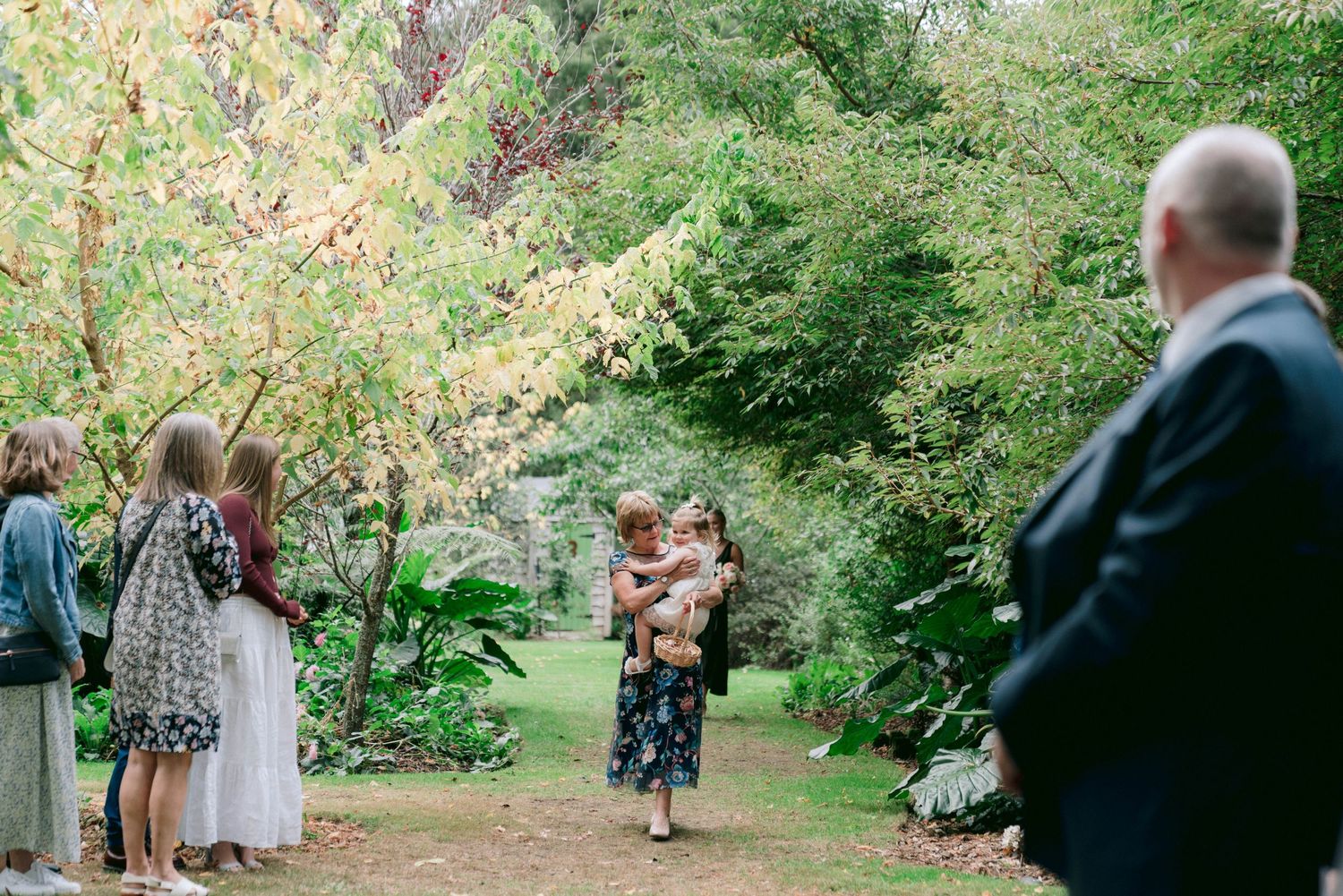Garden wedding reception with guests gathered under trees at sunset.