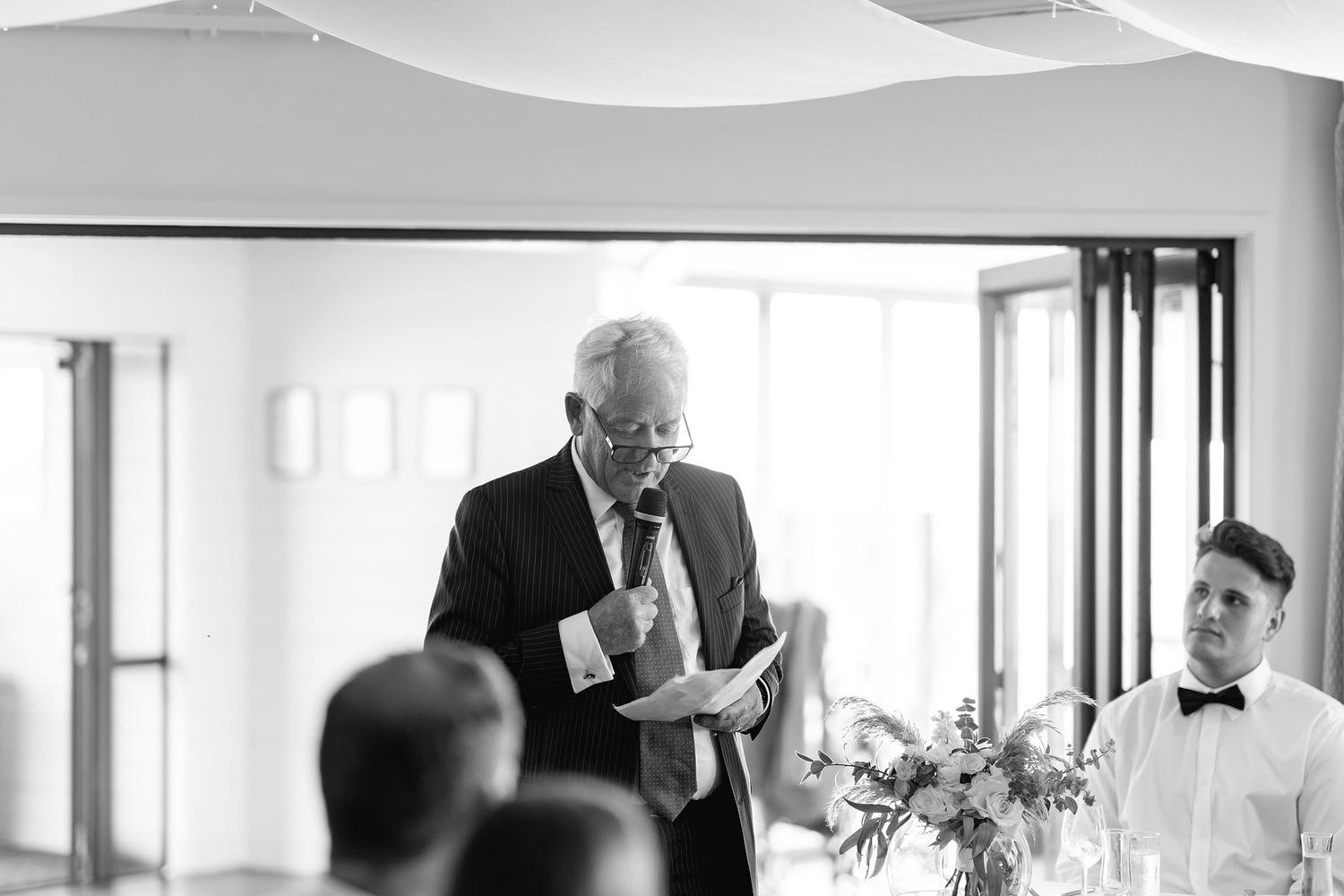 A black and white photograph of someone giving a heartfelt speech during a wedding reception.