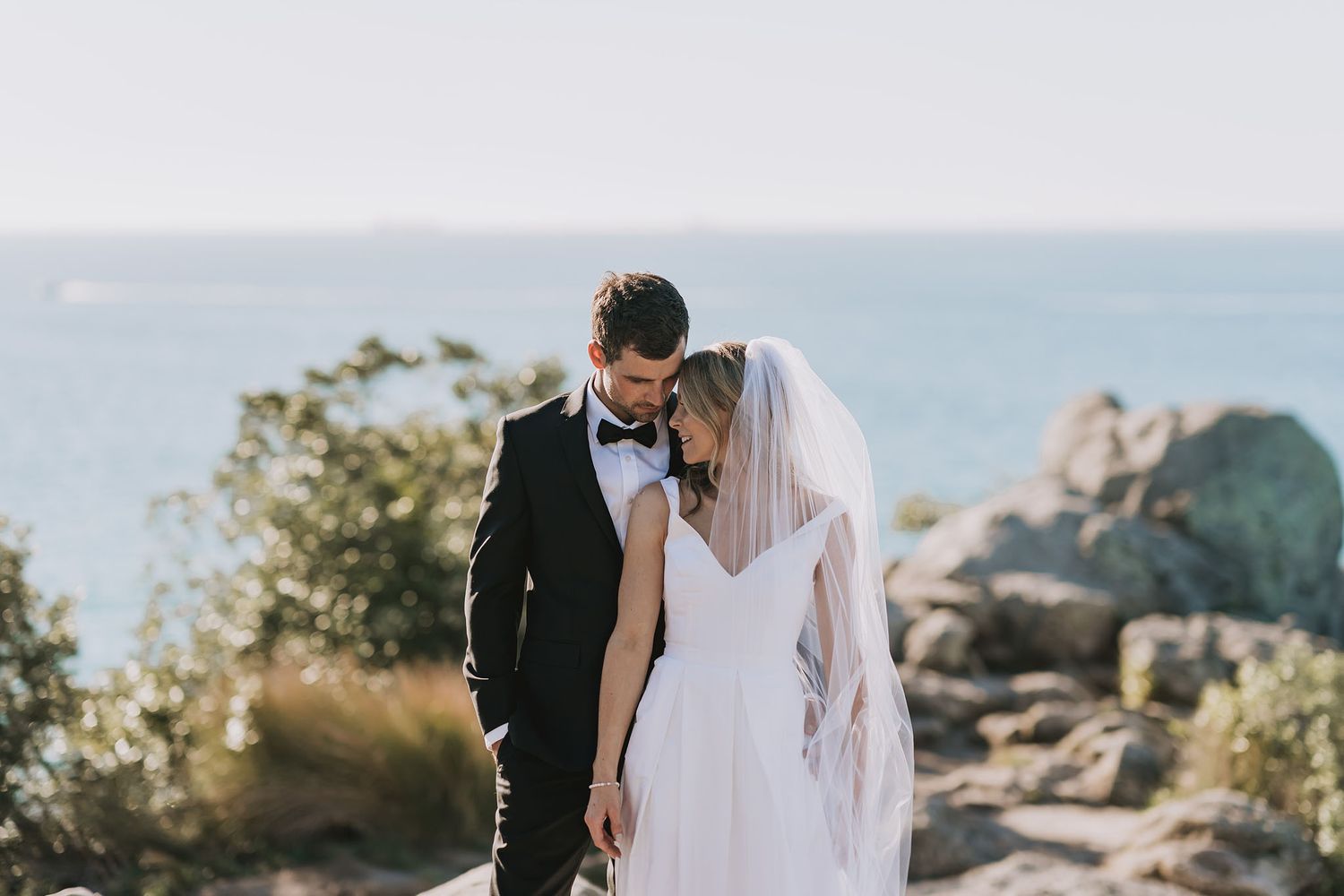 A couple in wedding attire stands together overlooking a scenic mountain landscape at sunset.