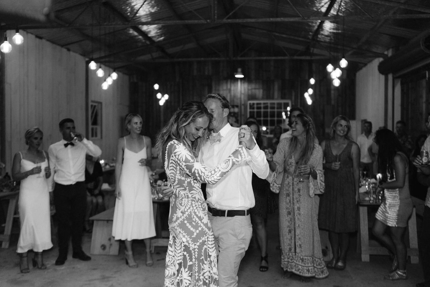 A couple slow dances in the middle of a reception venue while guests watch from the sides.