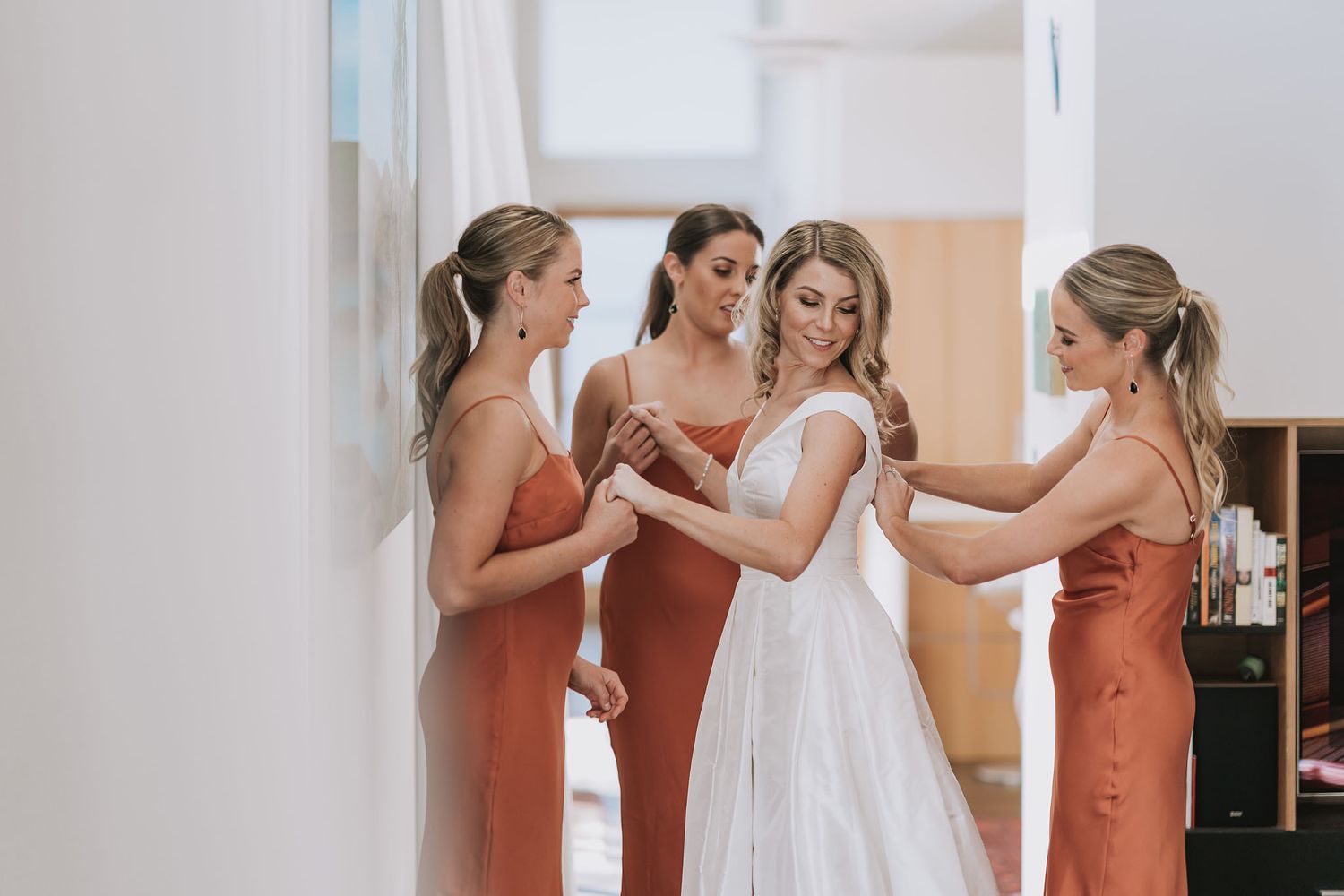 Bridesmaids in peach dresses help secure a bride's veil in an elegant getting-ready suite.