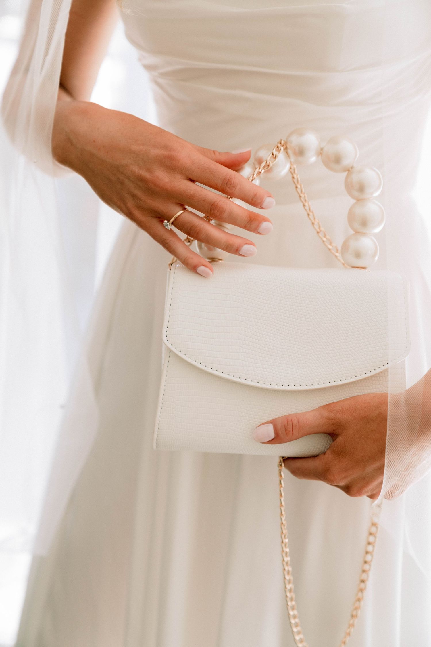 Close-up detail of bride's white handbag with pearl accents and delicate gold chain strap against wedding dress.