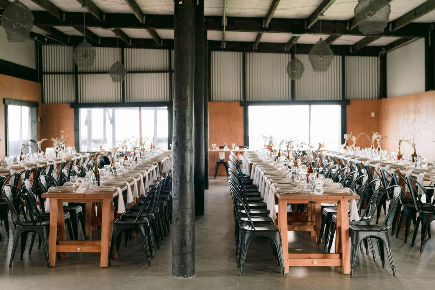 Long reception tables set with place settings in an industrial-style venue with exposed beams.