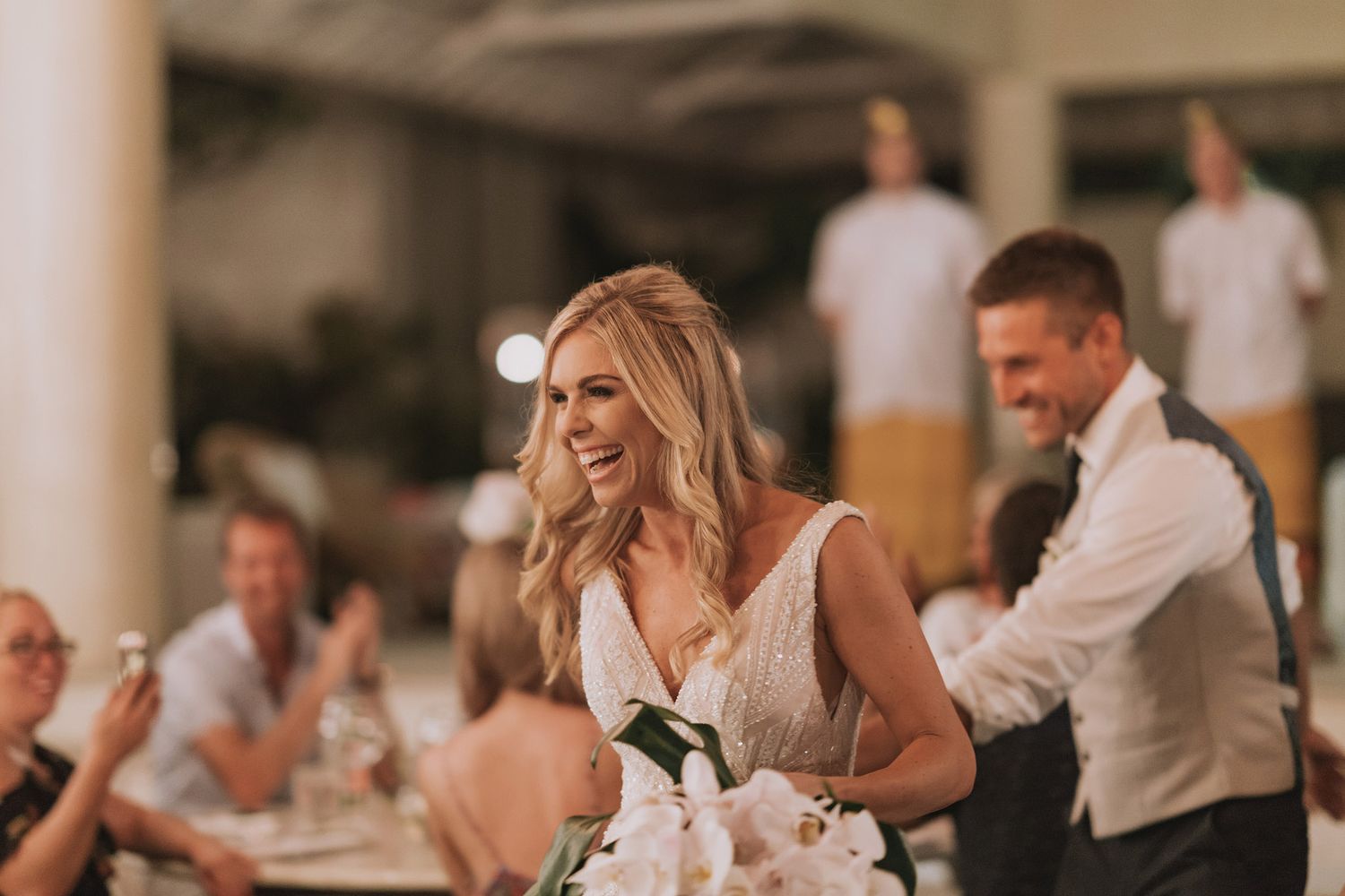 Wedding reception guests celebrating and dancing inside an elegant covered venue with white columns.