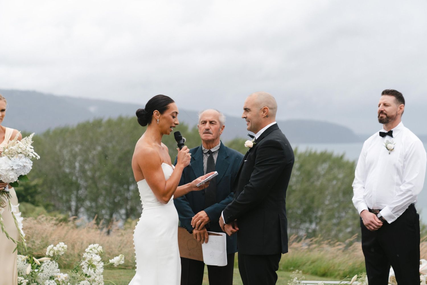 A couple smiles joyfully during their outdoor mountain wedding ceremony with an officiant.